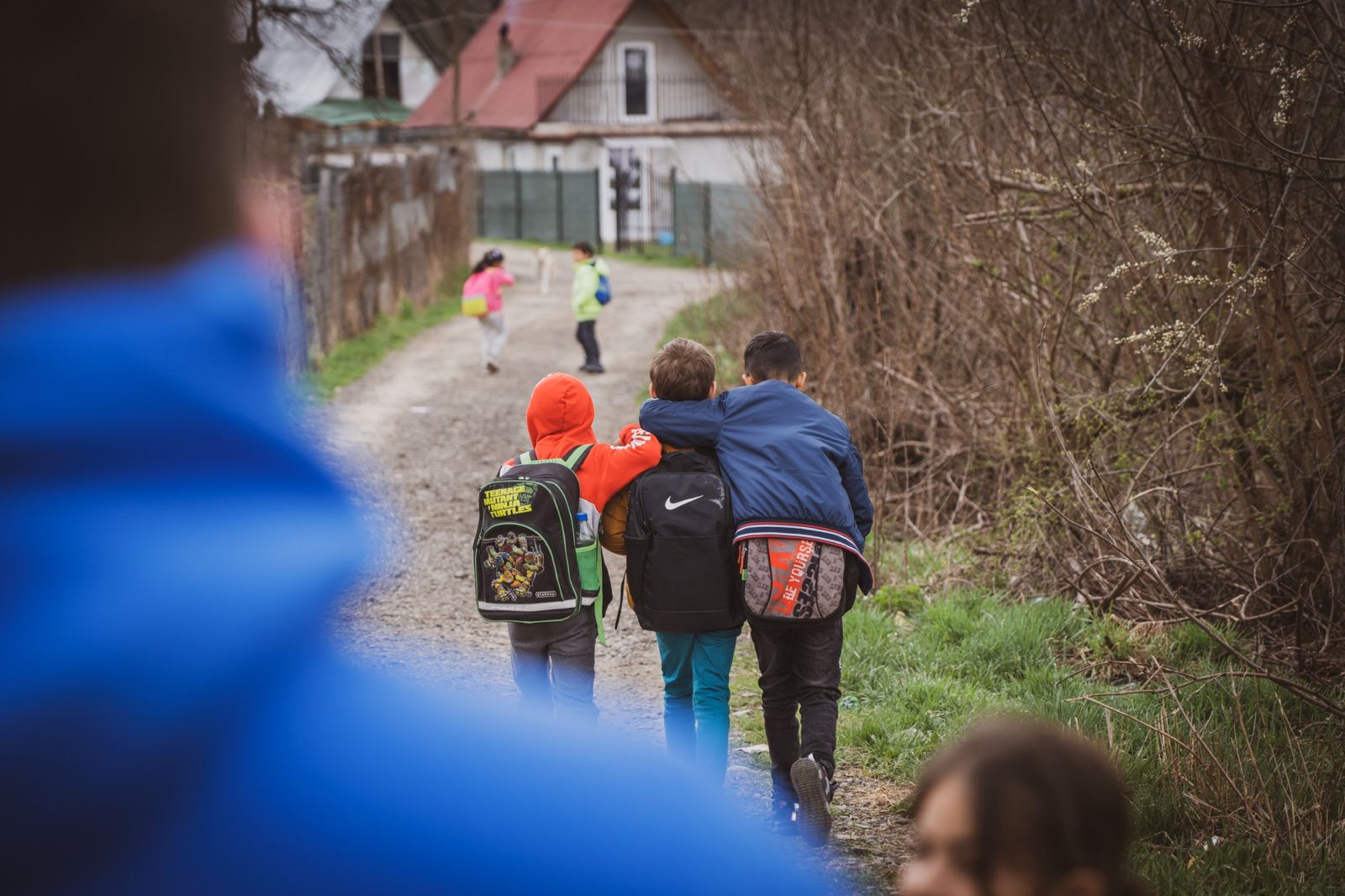 Children with backpacks walking away up a village lane