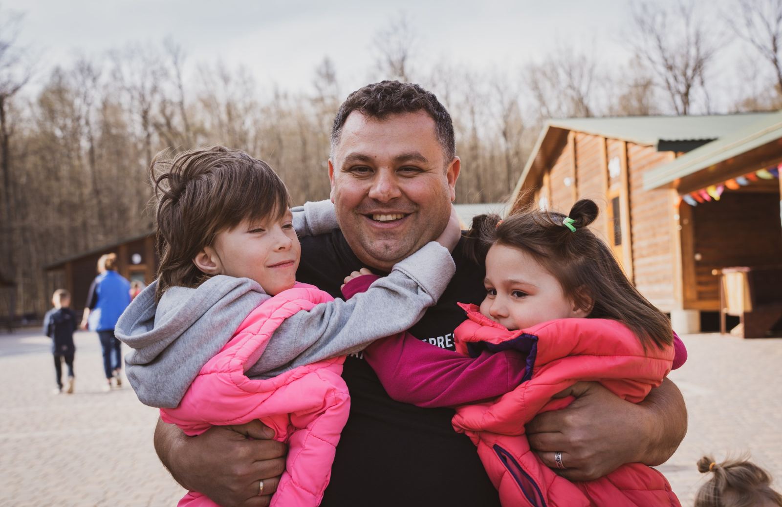 A staff member carrying two small girls in pink coats outside the centre