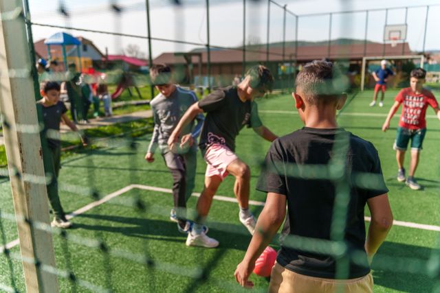 Children playing football on the astroturf pitch, seen through the netting